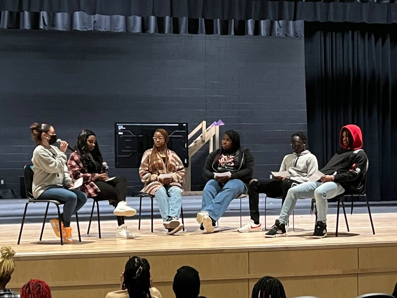 A group of students and a moderator on stage speaking at a panel.