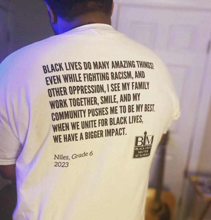 Steering Committee member wearing 2023 Week of Action t-shirt. The back reads the artist statement, "Black Lives do many amazing things! Even while fighting racism, and other
oppression, I see my family work together, smile, and my community pushes me to be my best. When
we unite for Black lives, we have a bigger impact."